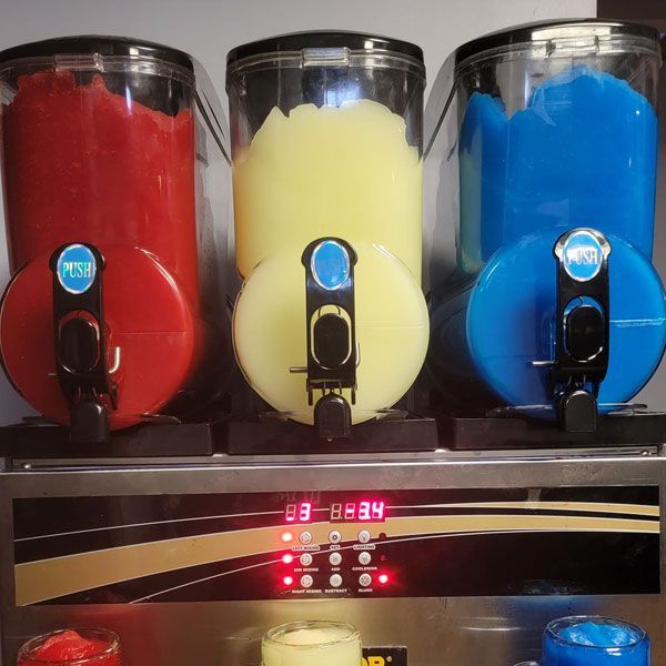 Three containers of different flavors of slushy are lined up on a shelf.