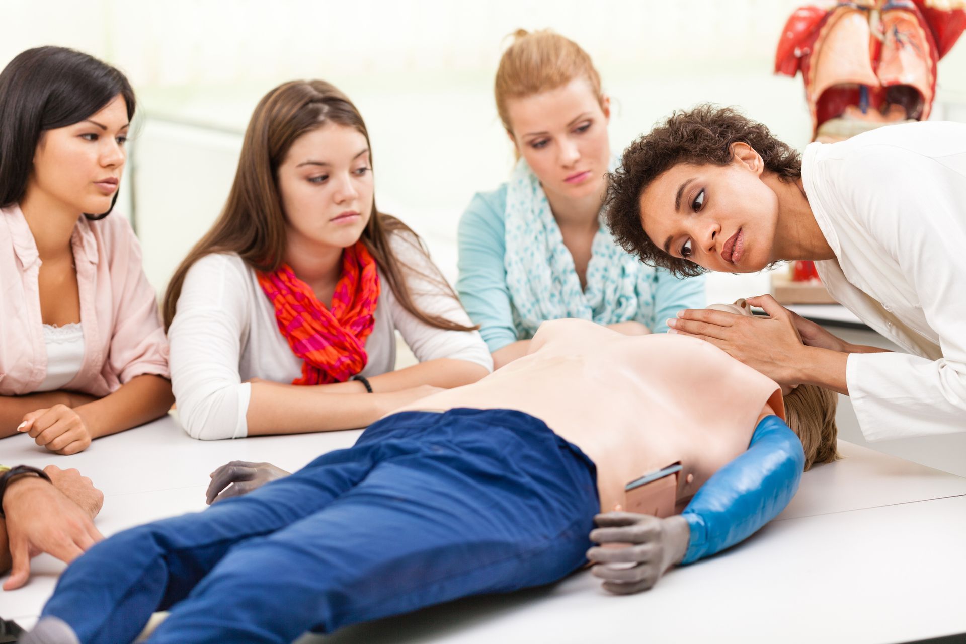 Two women are practicing first aid on a mannequin.