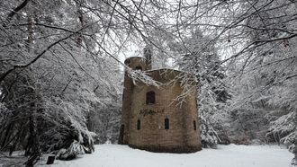 Stenen toren in een besneeuwd bos. Bomen die met sneeuw bedekt zijn, omringen het bouwwerk.
