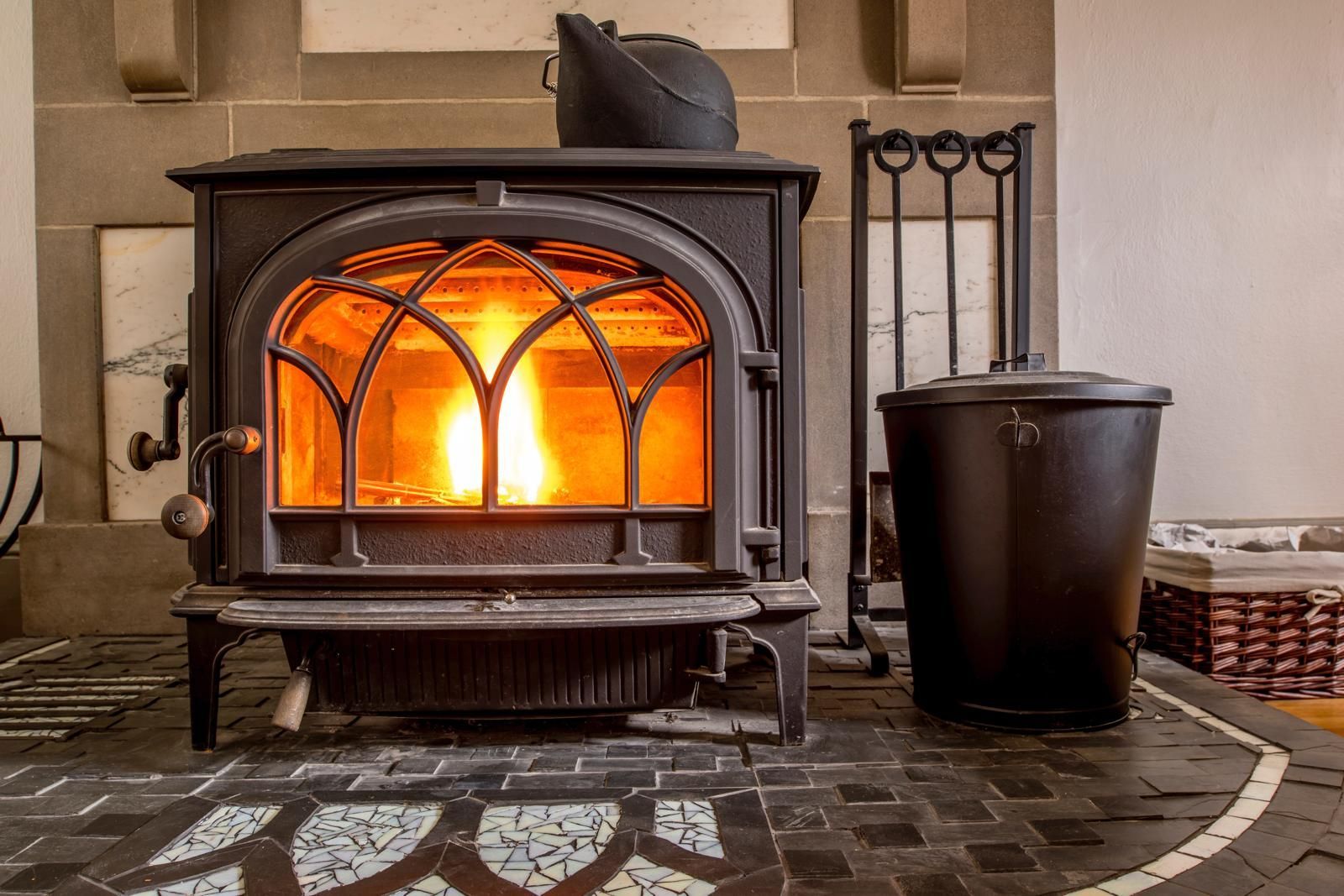 A wood-burning stove with a roaring fire, next to a coal bucket, in a cozy room.
