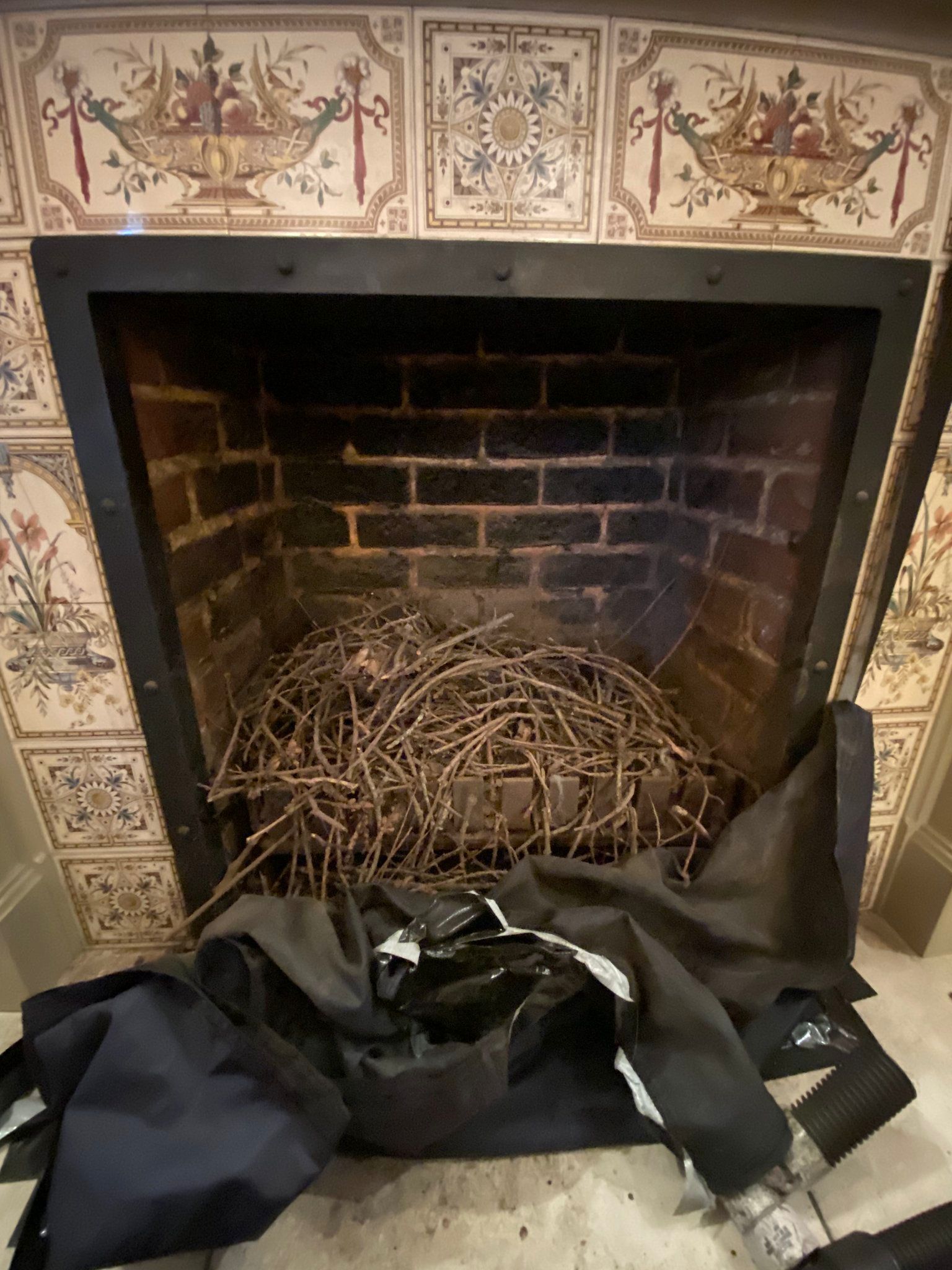 A fireplace with a pile of twigs inside, with a black garment or bag in front of it. 