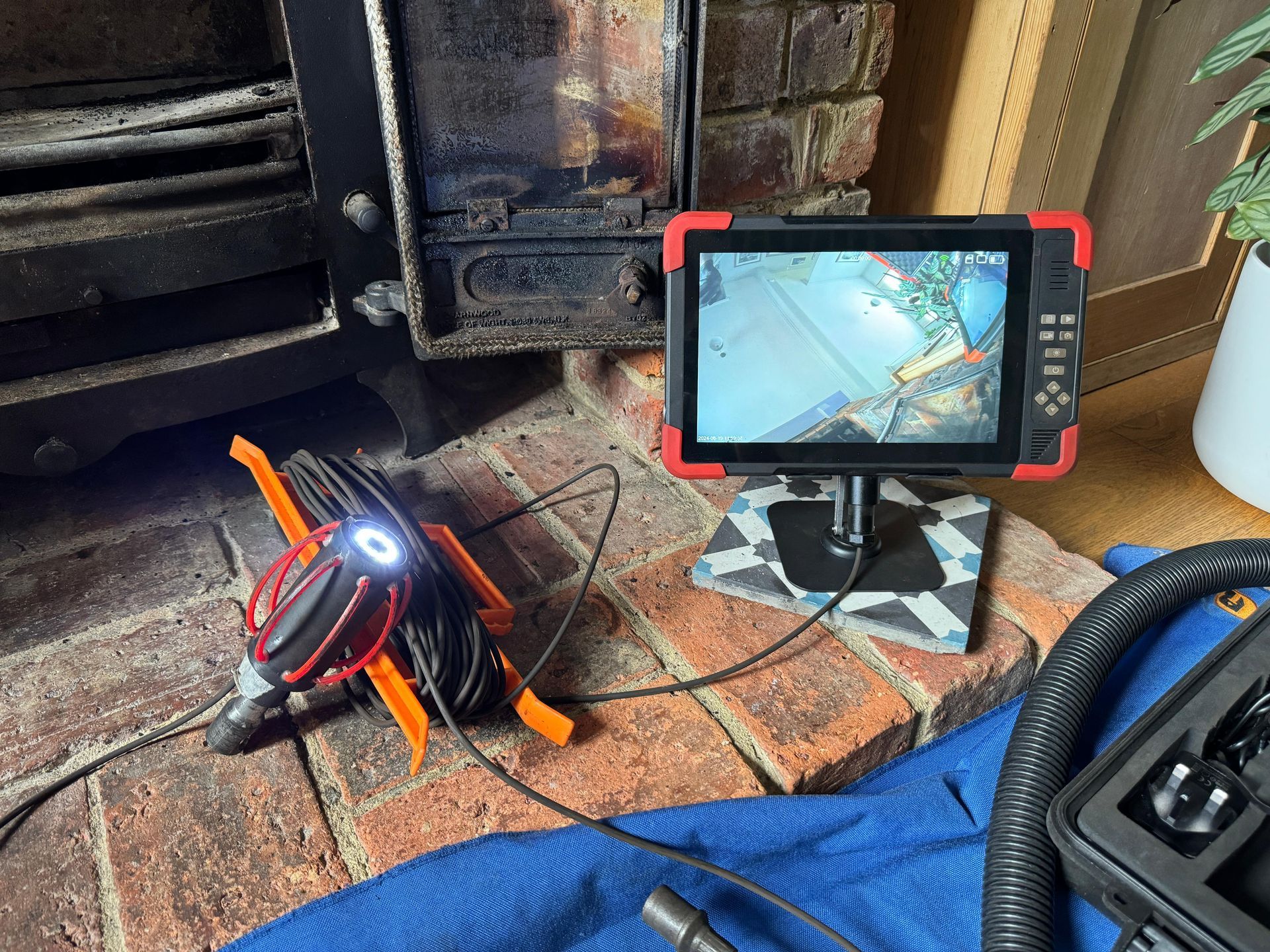 A chimney inspection camera on a brick hearth, showing a screen displaying a view, with the camera unit beside the fireplace.