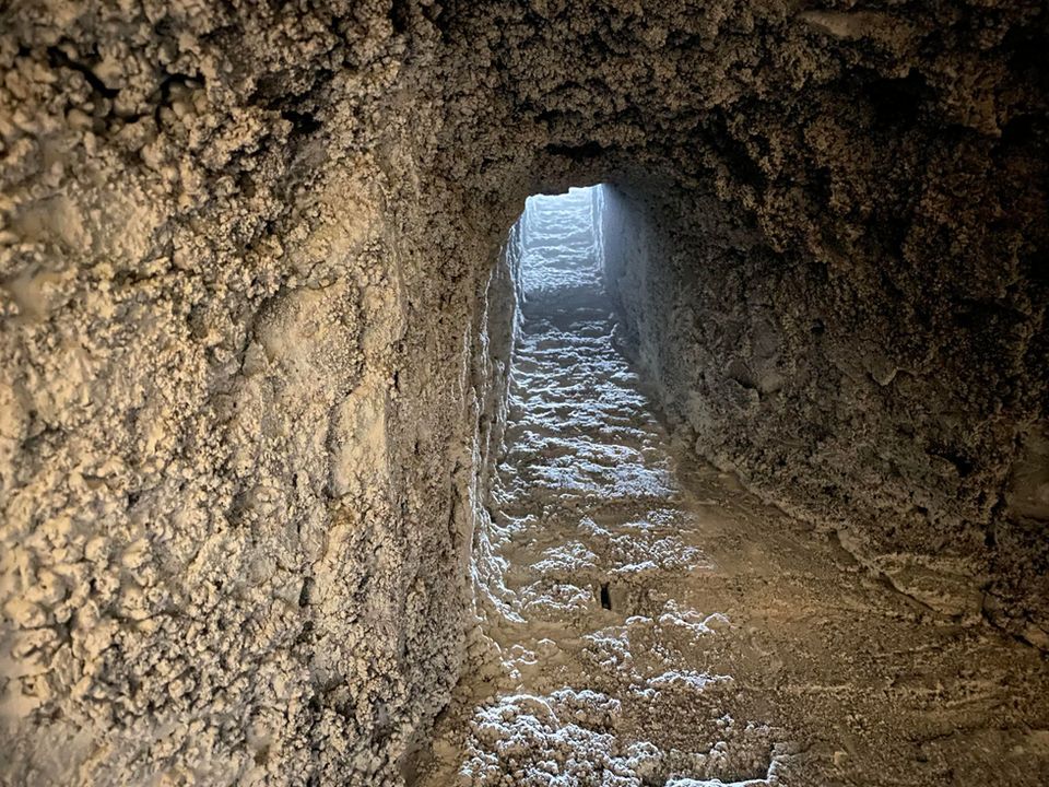 A narrow, dimly lit tunnel with rough, textured walls and a light source at the end.