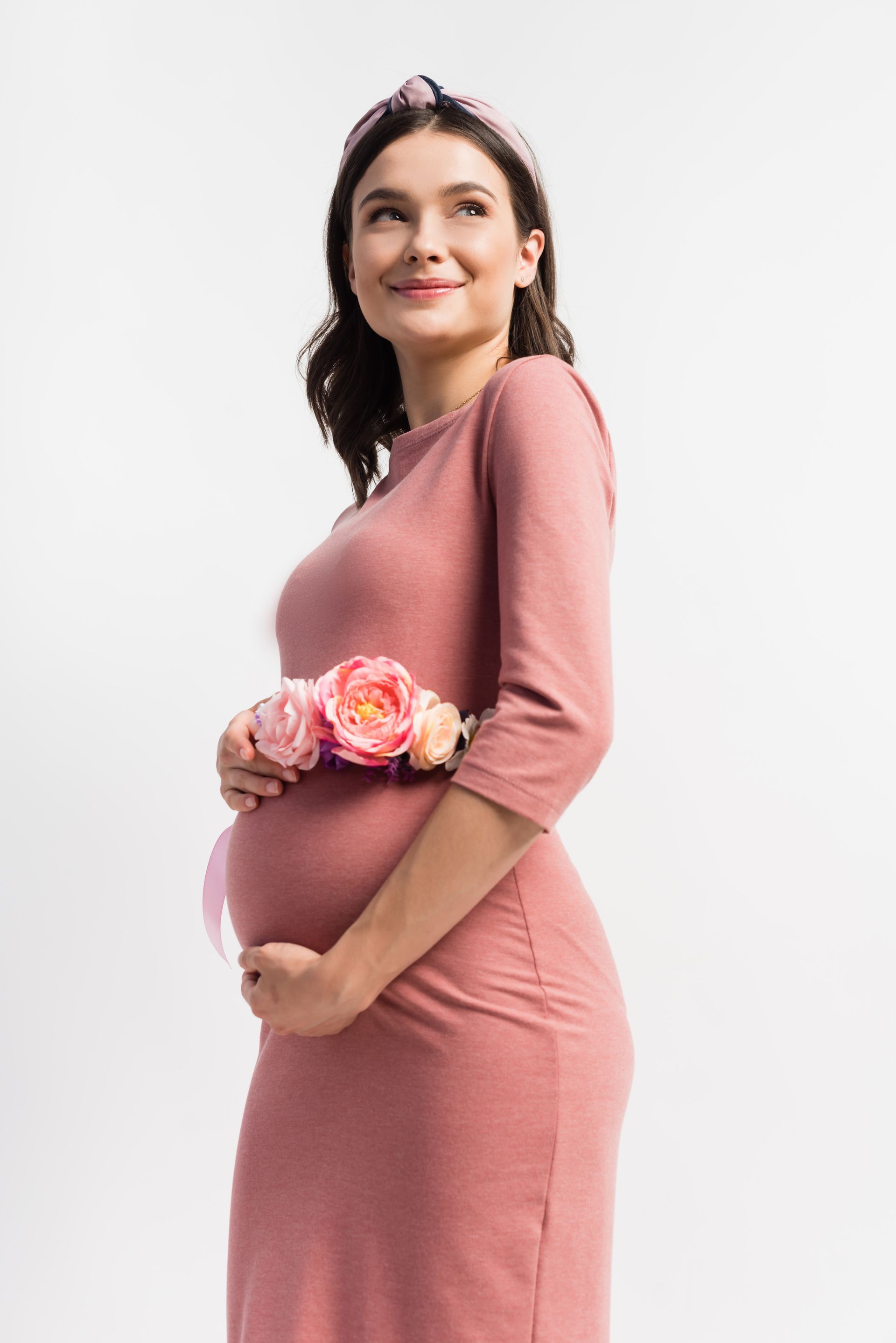 A pregnant woman in a pink dress is holding a flower around her waist.