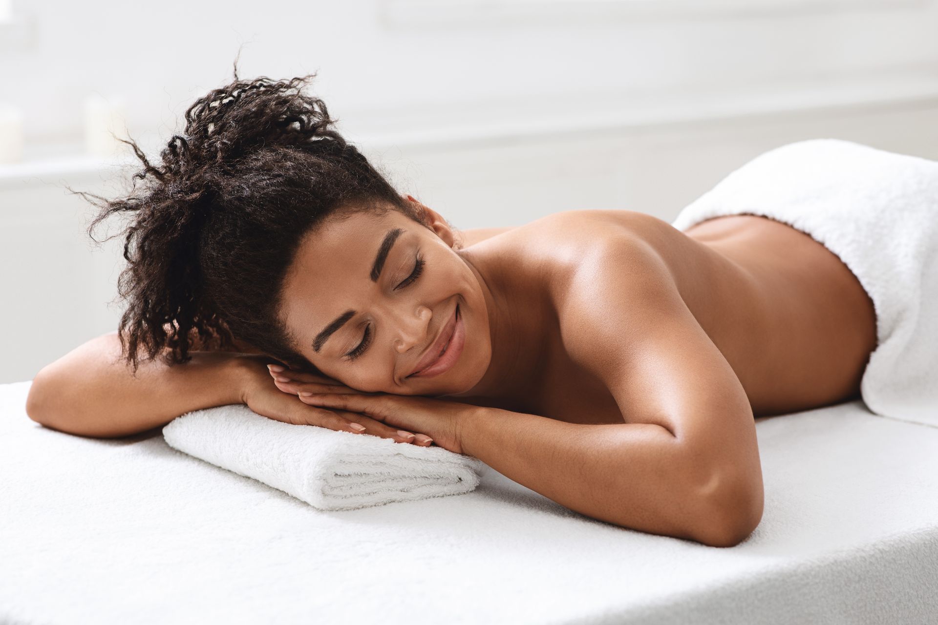 A woman is laying on a massage table with her eyes closed and smiling.