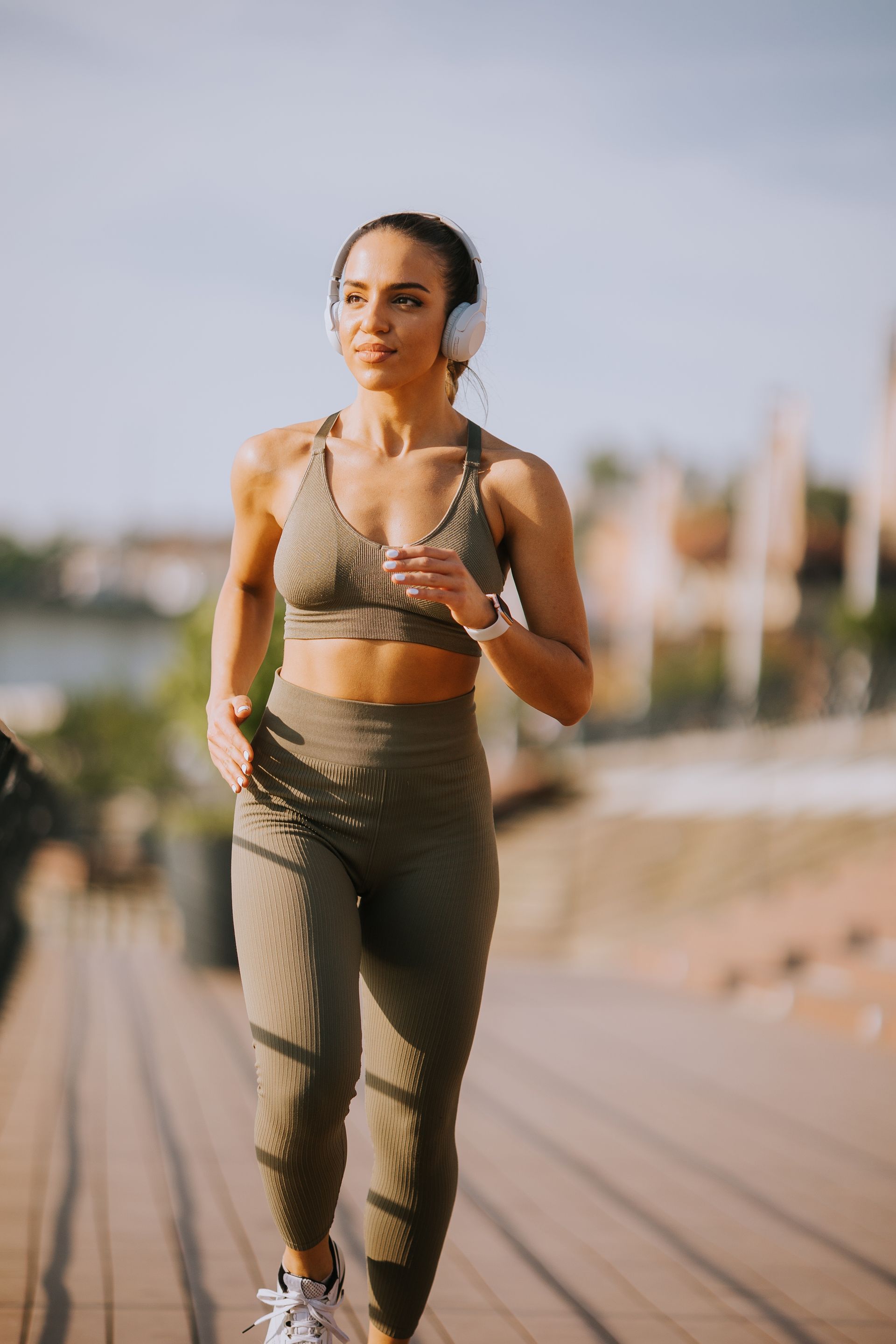 A woman wearing headphones is running on a pier.