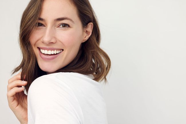 A woman in a white shirt is smiling and looking over her shoulder.