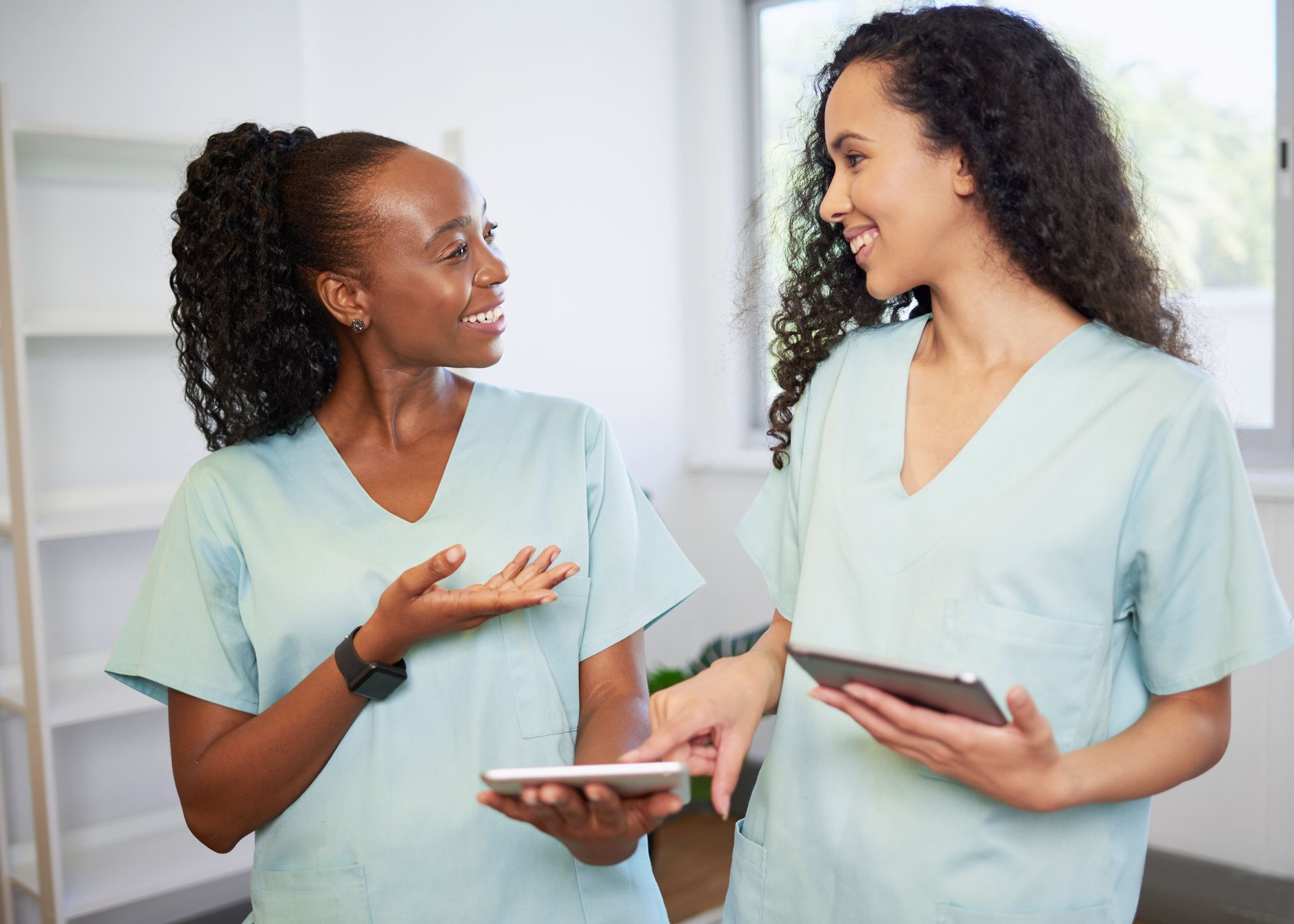 Two nurses are standing next to each other and looking at a tablet.