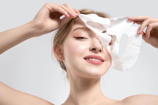 A woman is applying a sheet mask to her face.