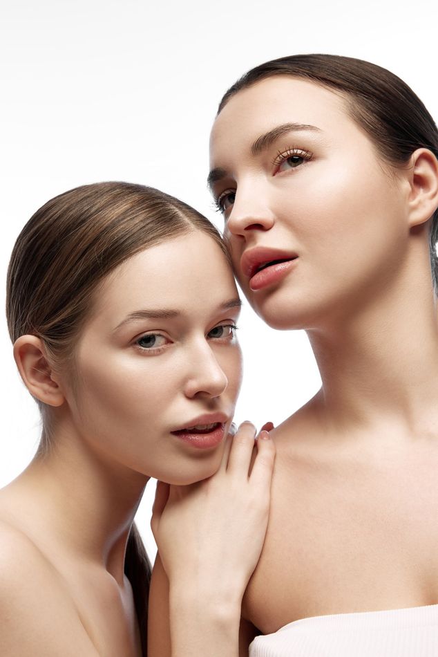 Two women are standing next to each other on a white background.