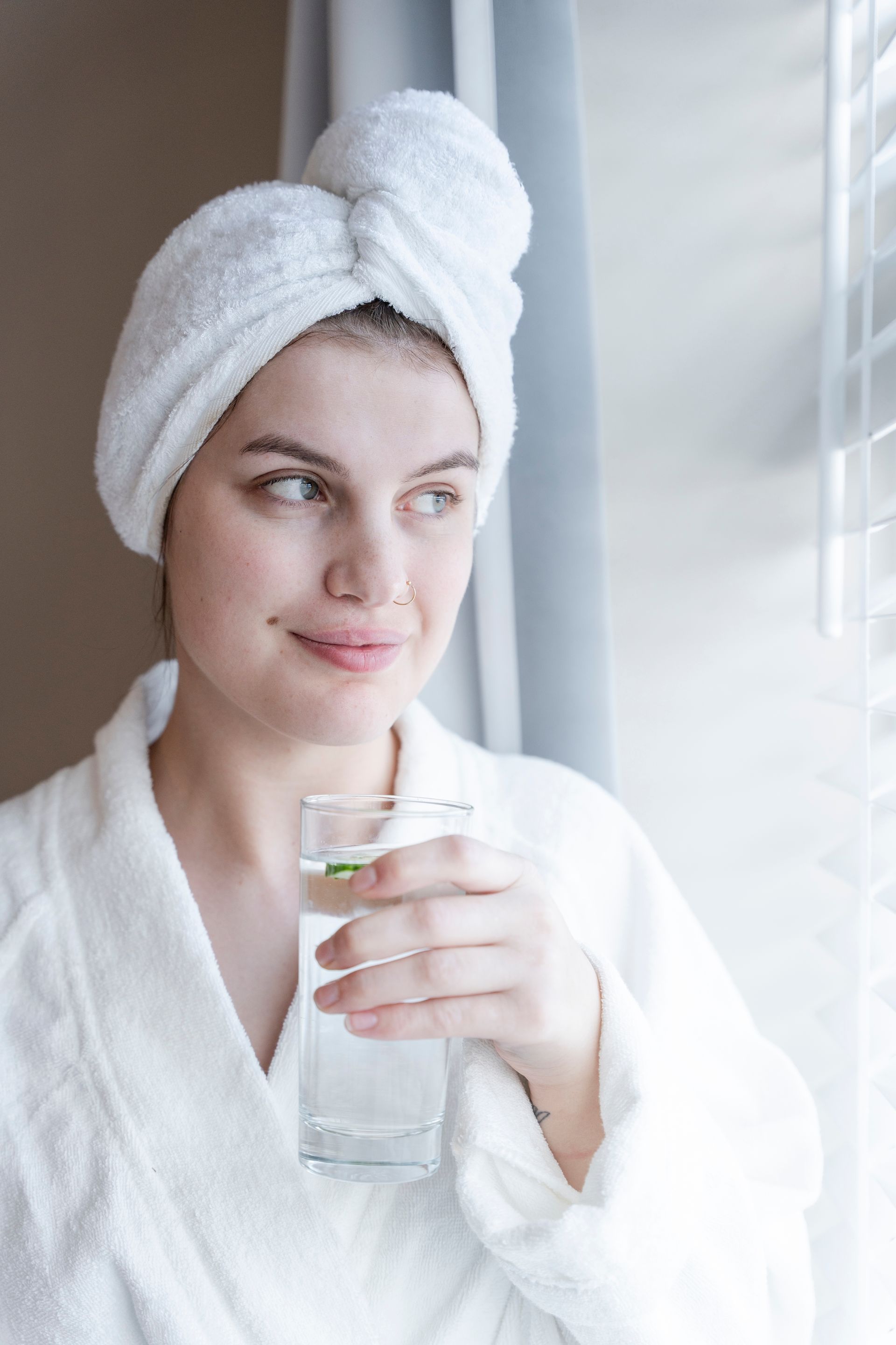 A woman with a towel wrapped around her head is drinking a glass of water.