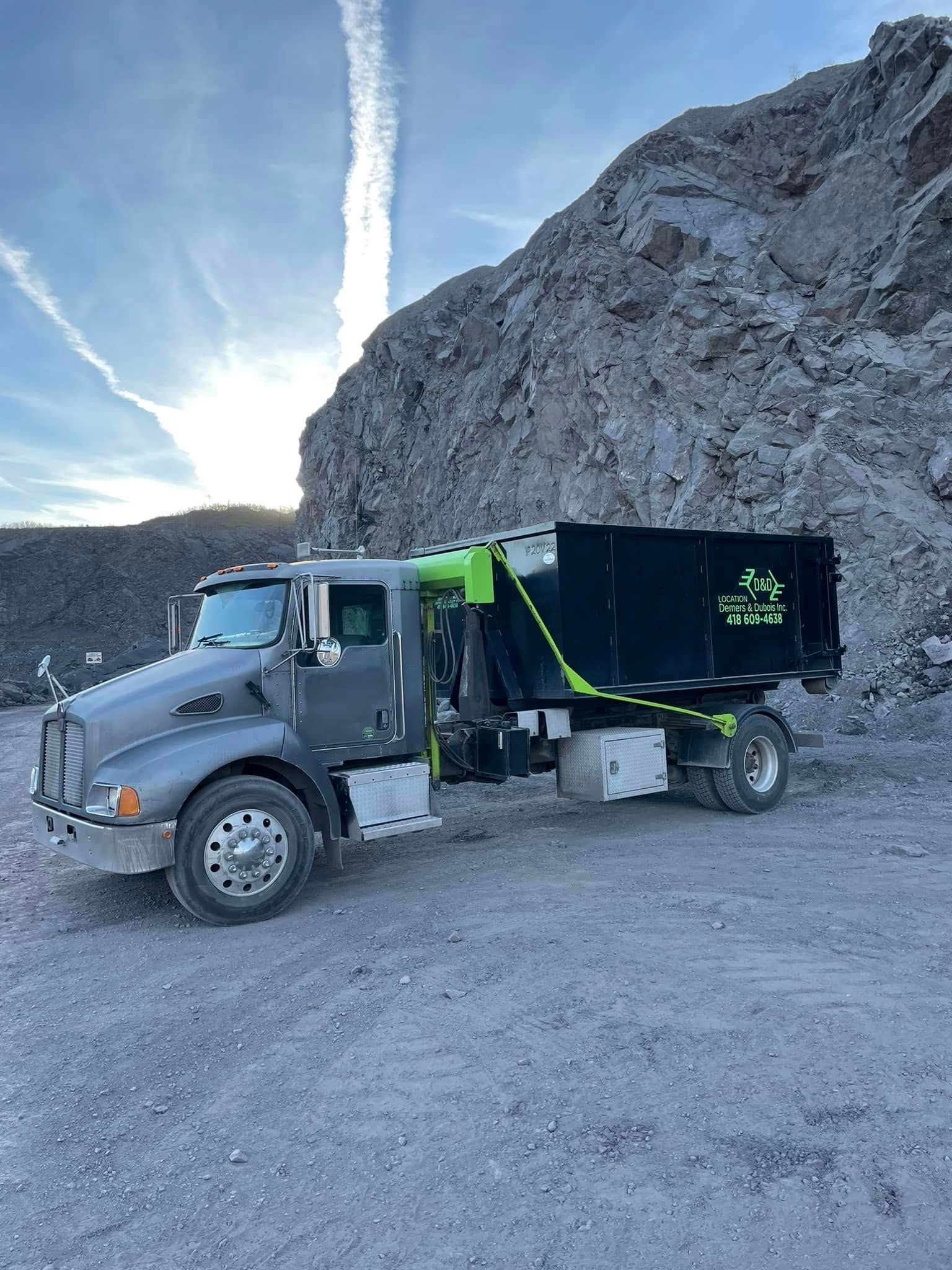 Camion à benne basculante gris avec des accents noirs et verts dans une carrière avec un fond rocheux.