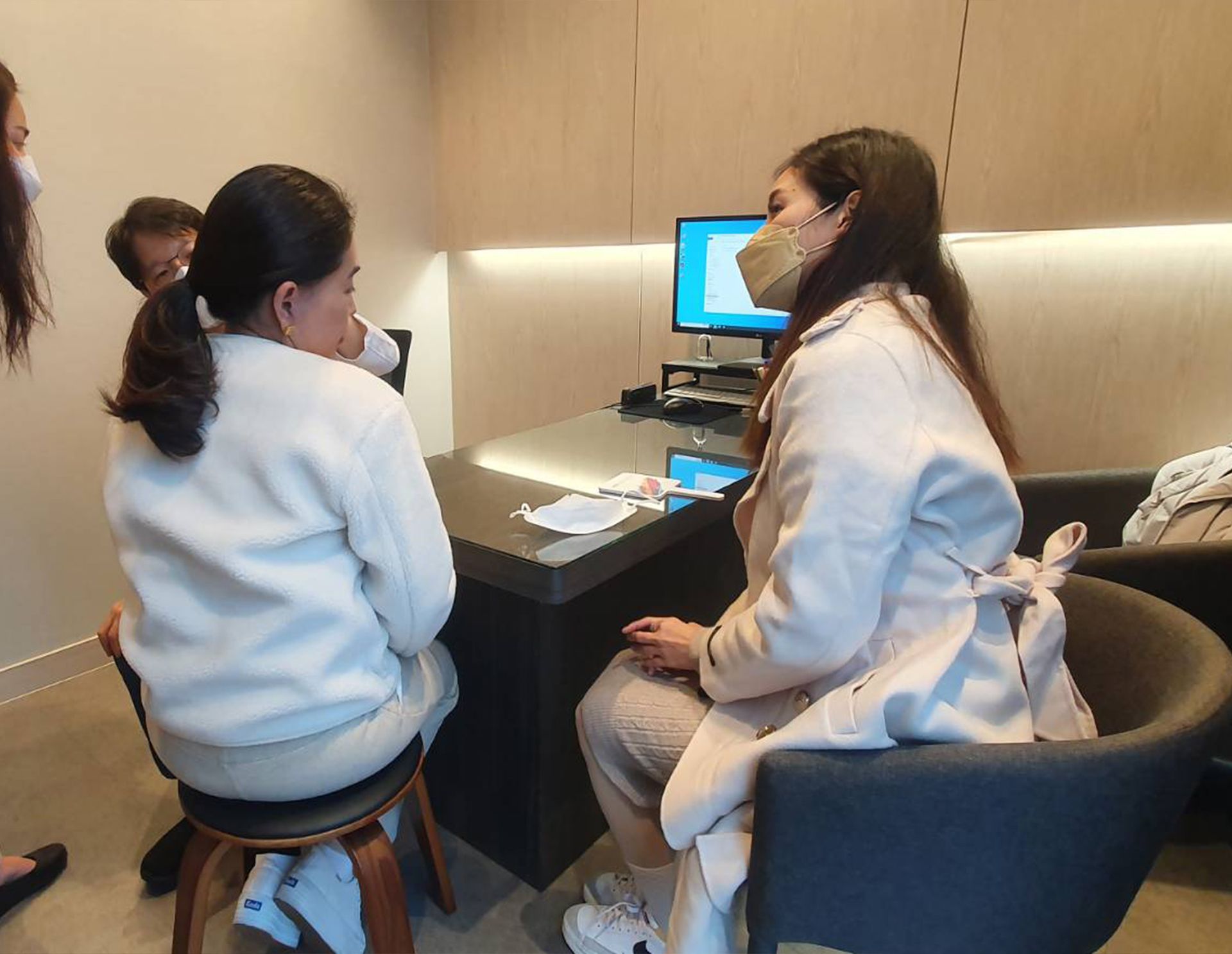 Two women seated in an office, one wearing a mask, looking at a computer.
