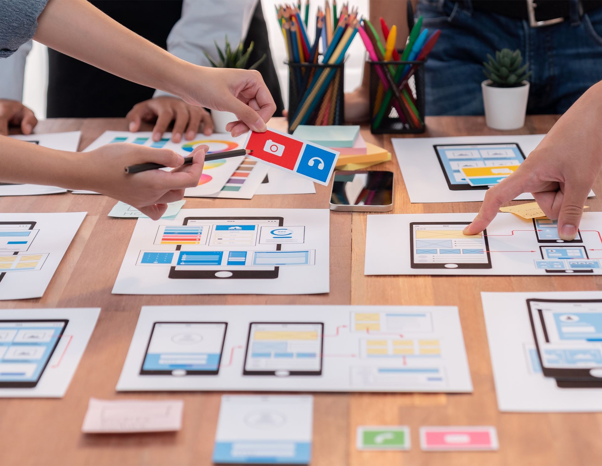 People collaborating on mobile app design, using sketches, icons, and diagrams on a table.