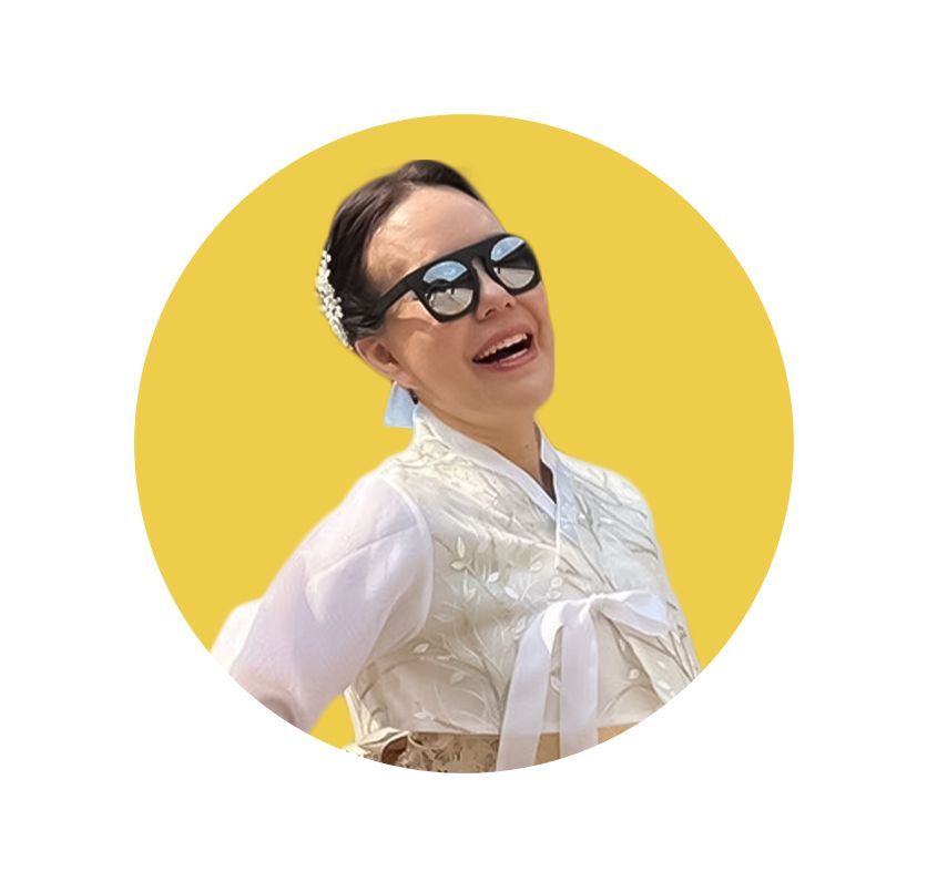 Woman in traditional Korean clothing and sunglasses, smiling broadly, yellow background.