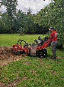 A man is standing next to a stump grinder in a yard.