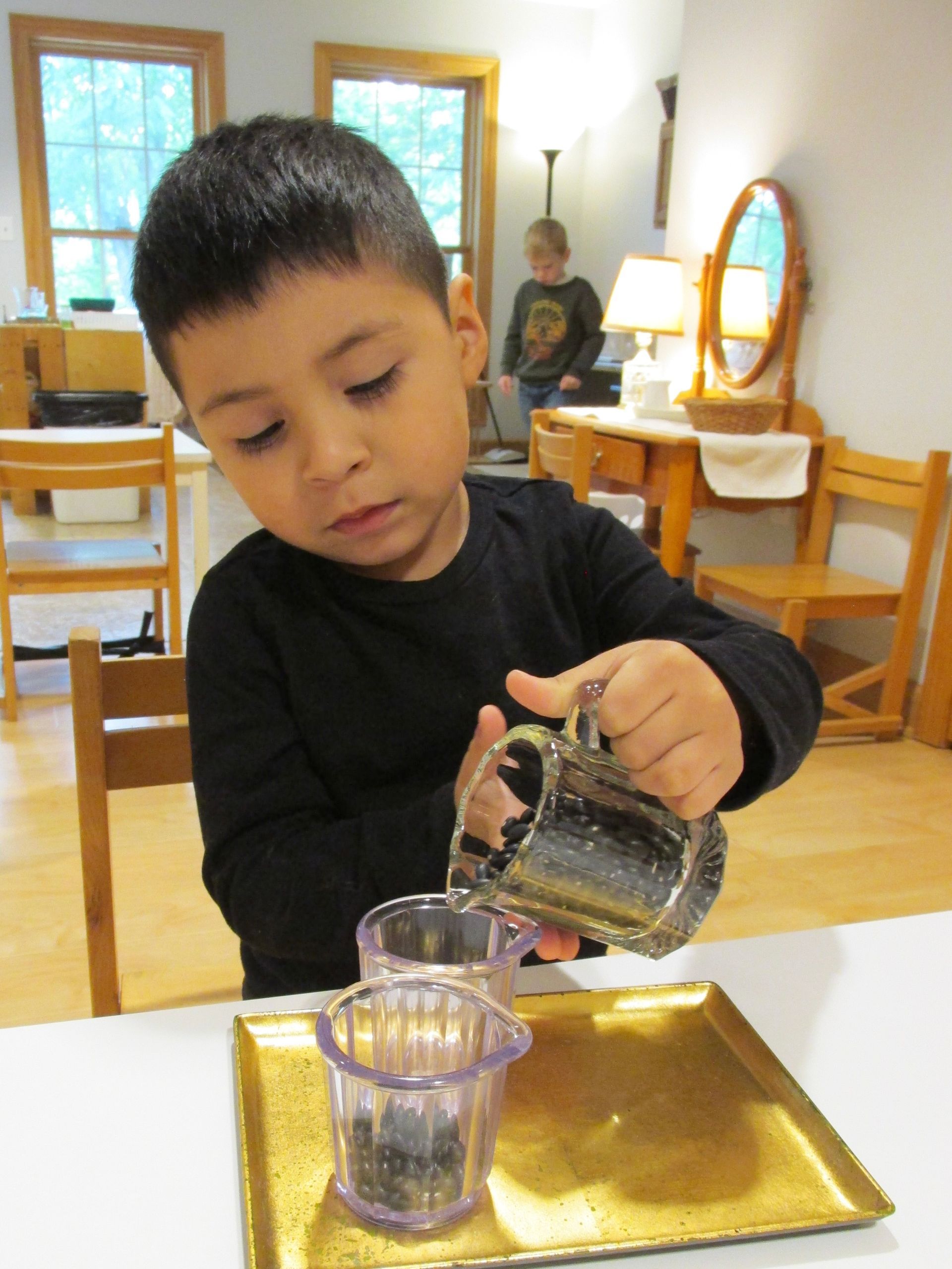 A Montessori primary child playing with jug and glass