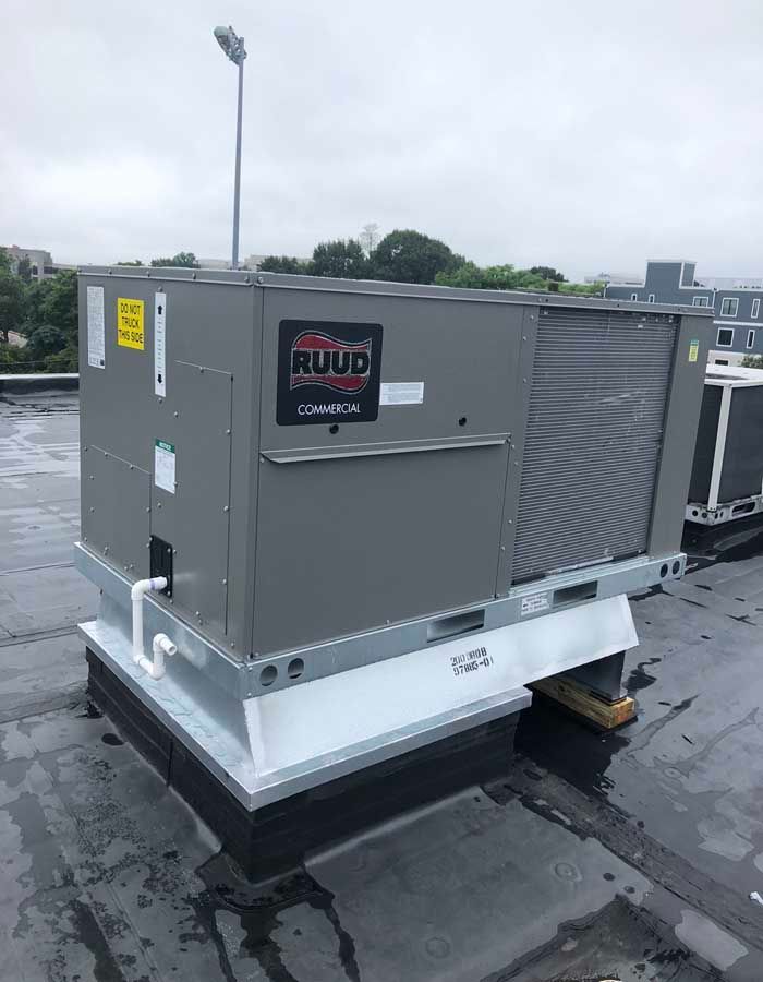 Rooftop HVAC unit with Ruud logo on a flat, wet roof.