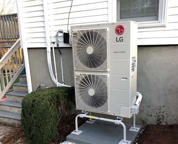 LG air conditioner unit installed on a white house exterior, near a bush and stairs.