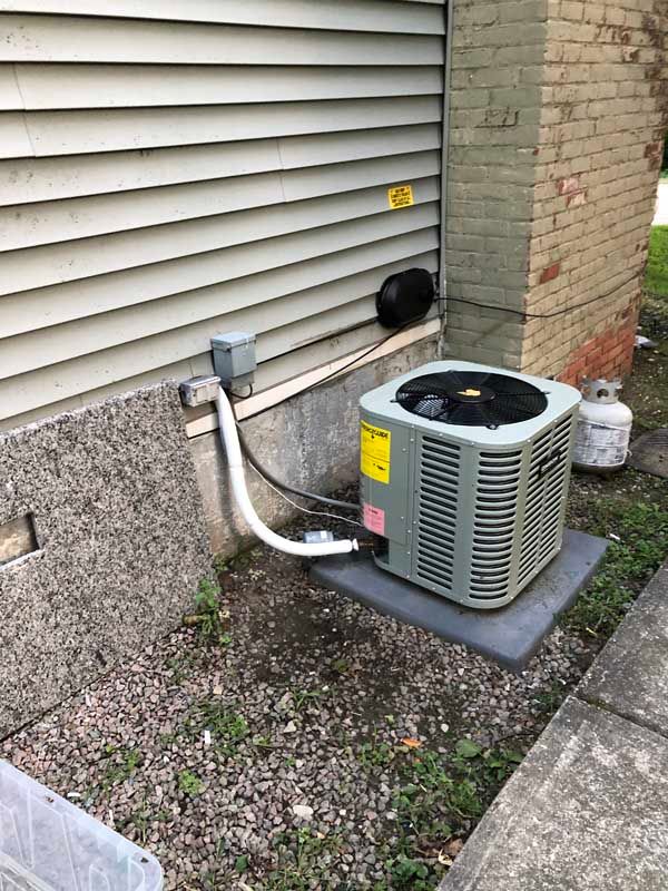 An air conditioning unit outside a house with gray siding, a propane tank, and gravel.