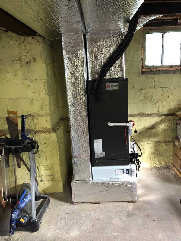 Mitsubishi HVAC unit in a basement, connected to insulated ductwork and a window.