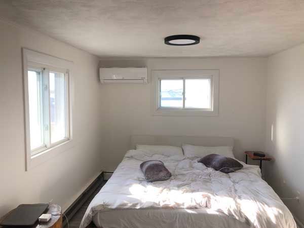 Bedroom with white walls, bed, and windows; air conditioning unit above bed.