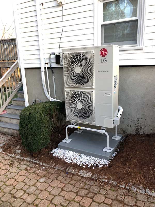 LG heat pump unit outside a house. White siding, gray base, and brick patio.