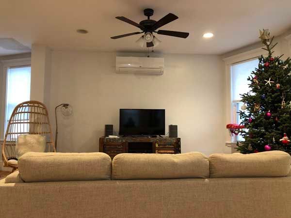 Living room with sofa, TV, Christmas tree, and ceiling fan; white walls, neutral tones.