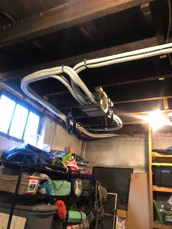 Basement ceiling with HVAC equipment, pipes, and storage. Dark wood beams and white pipes contrast.