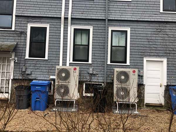 Two LG air conditioning units on a gray-shingled building, trash bins, and a white door.