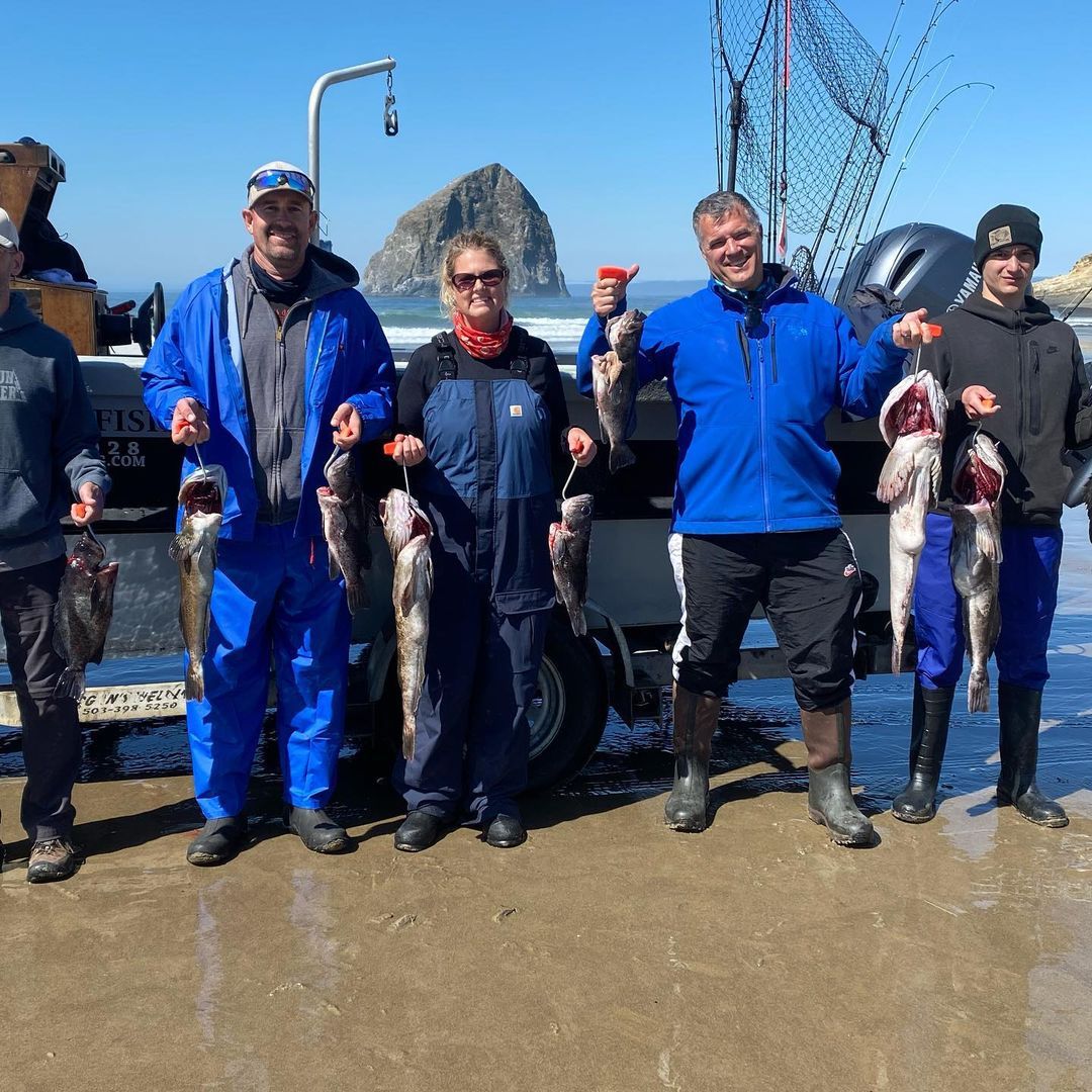 Group of people holding up freshly caught fish, near ocean, with a rocky background.