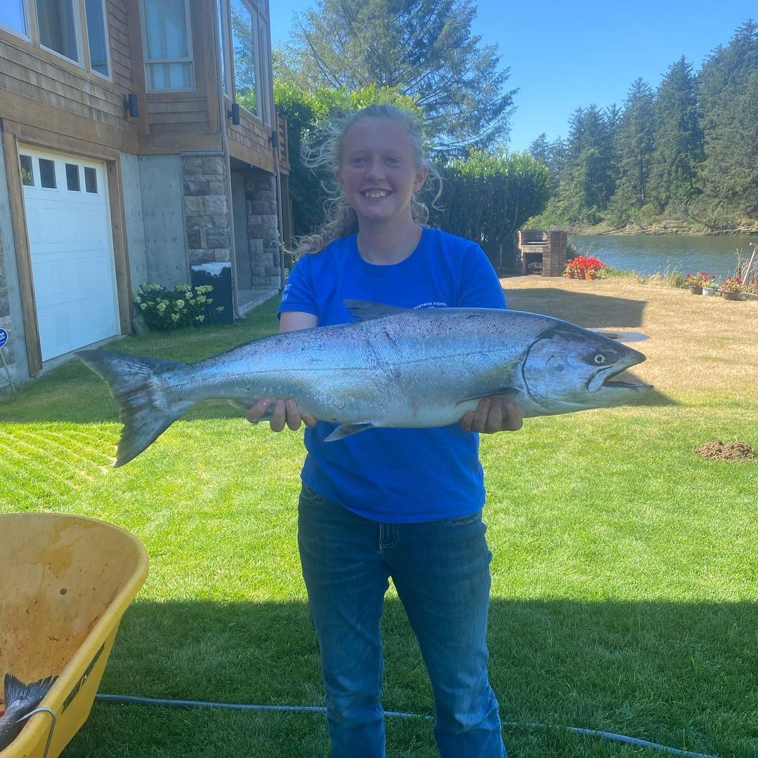 Woman in blue shirt holds a large fish in front of a house and yard.