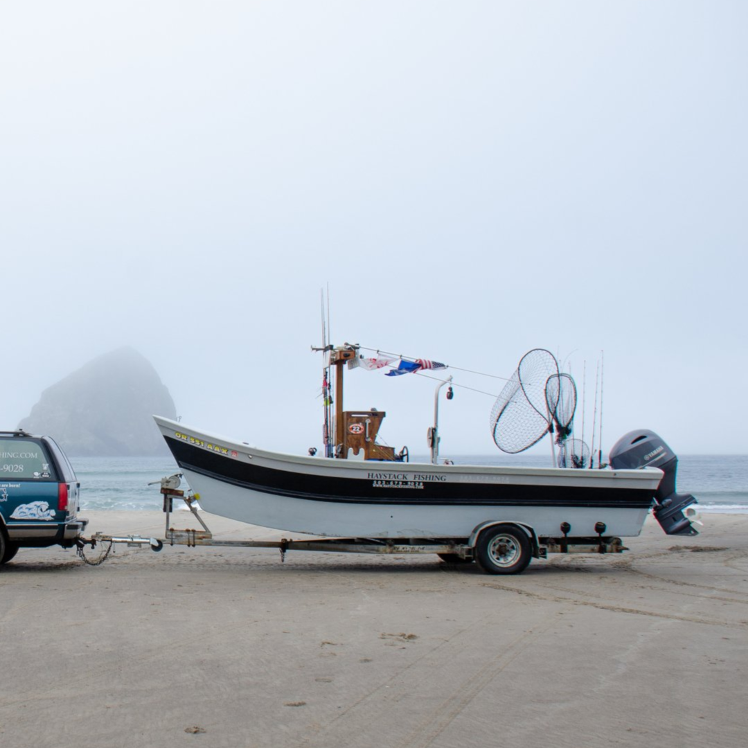 Boat on trailer being towed by a vehicle on a beach with a cloudy mountain background.
