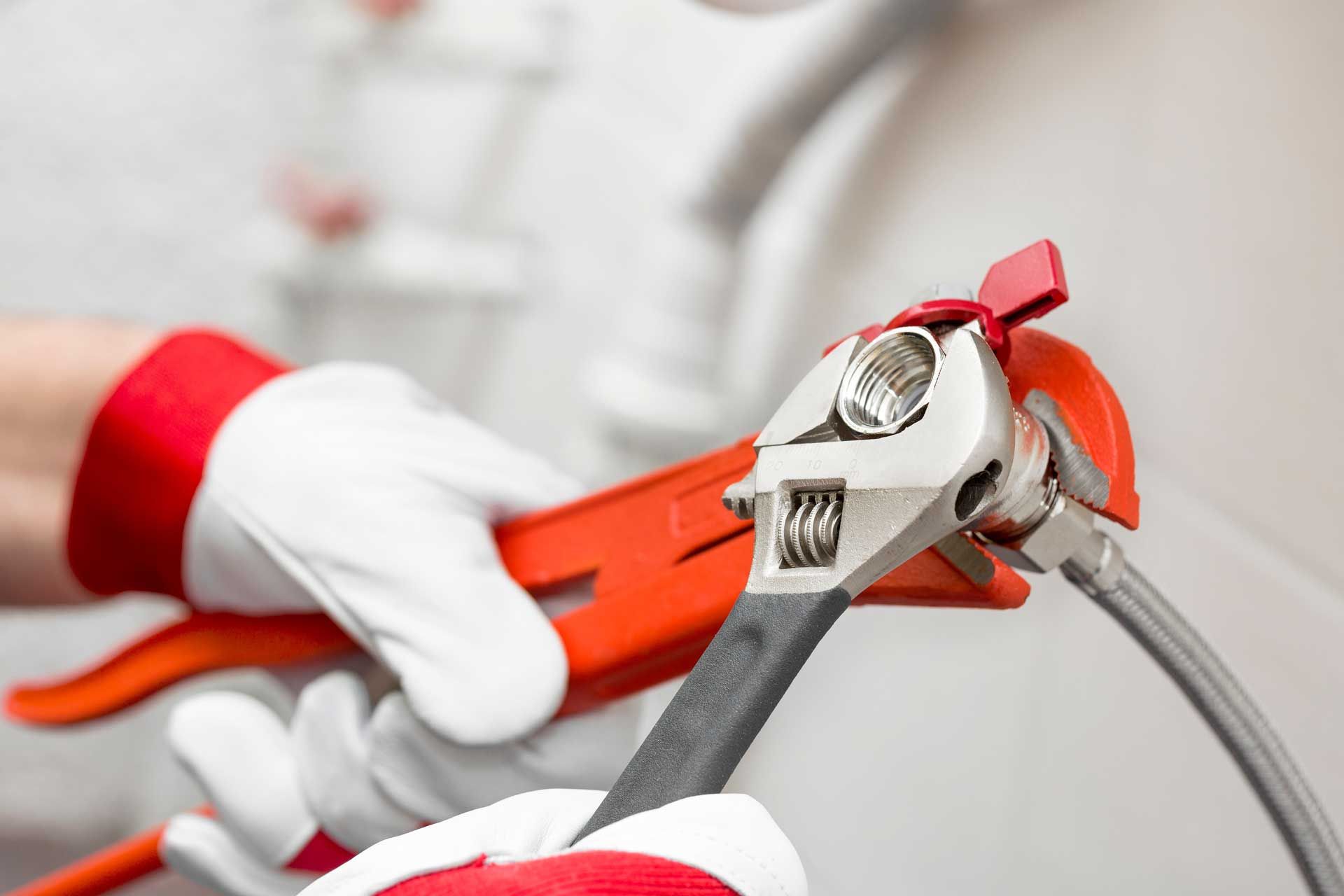 Gloved hands using a red pipe wrench to tighten a metal pipe connection