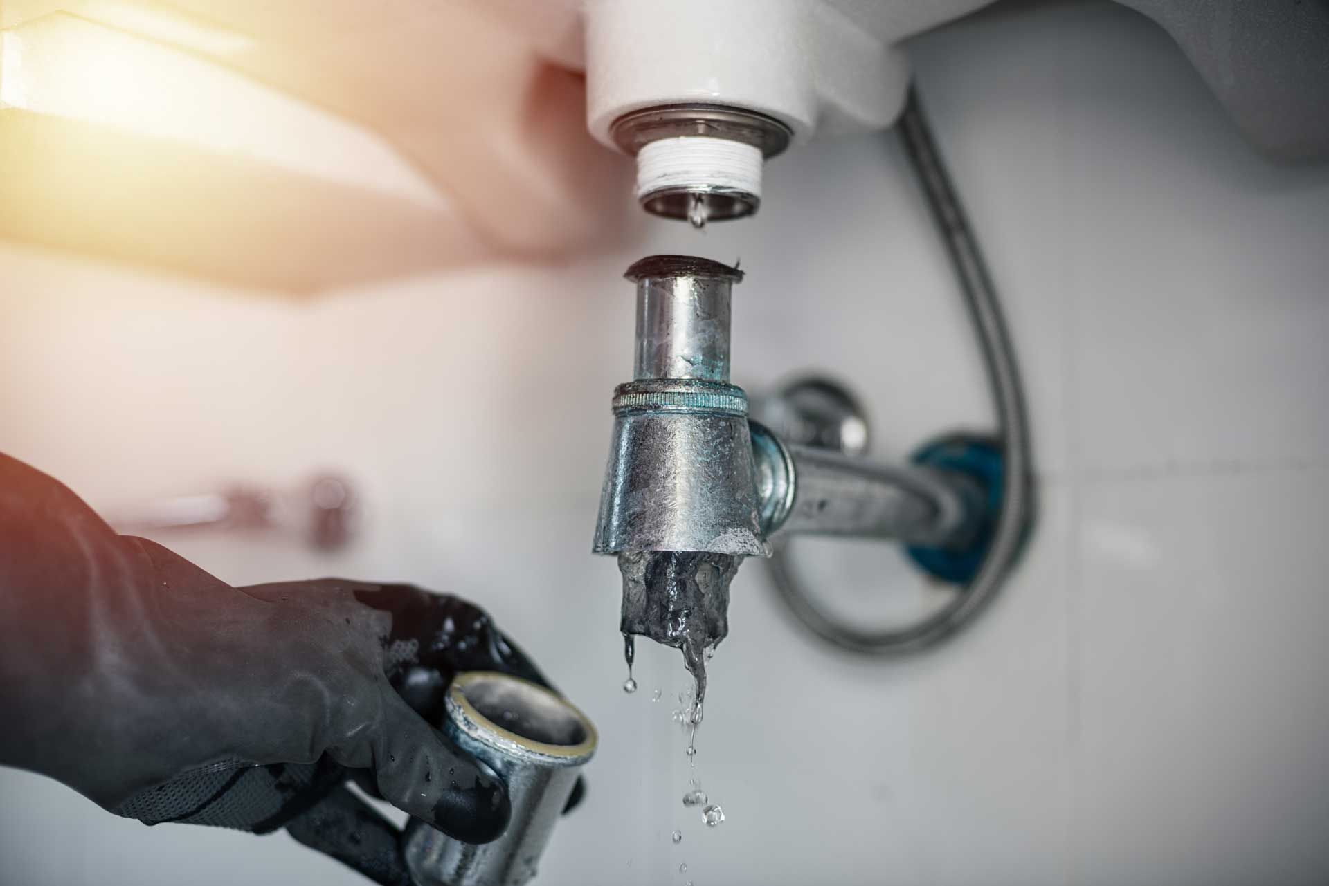 Hand turning off a running sink faucet with water dripping into a basin