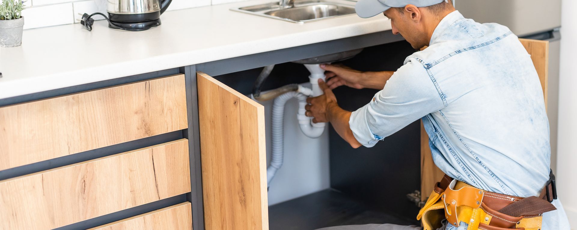 Plumber in blue overalls repairing a bathroom sink, with tools on the floor nearby