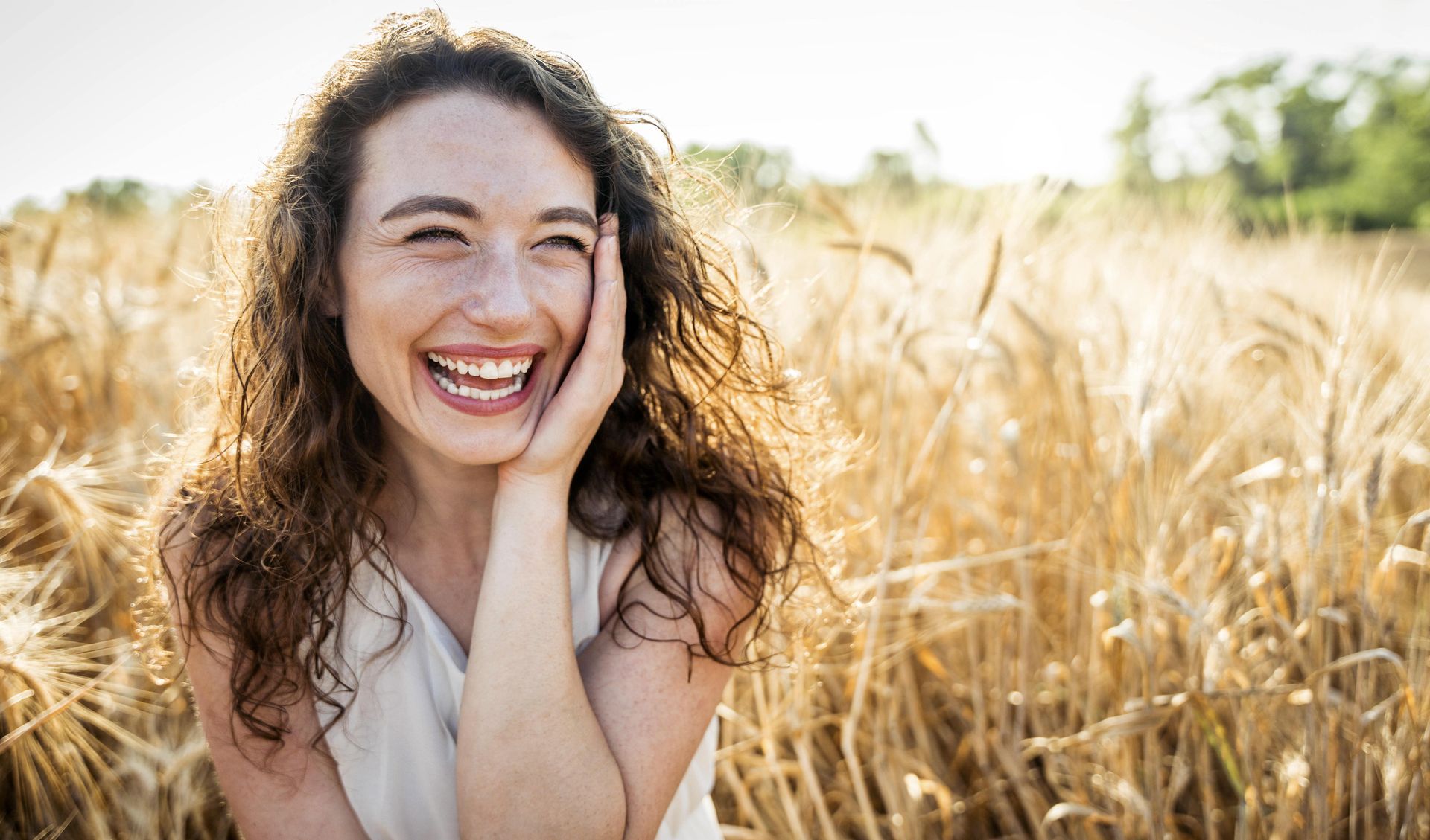 A woman is laughing in a field of wheat.