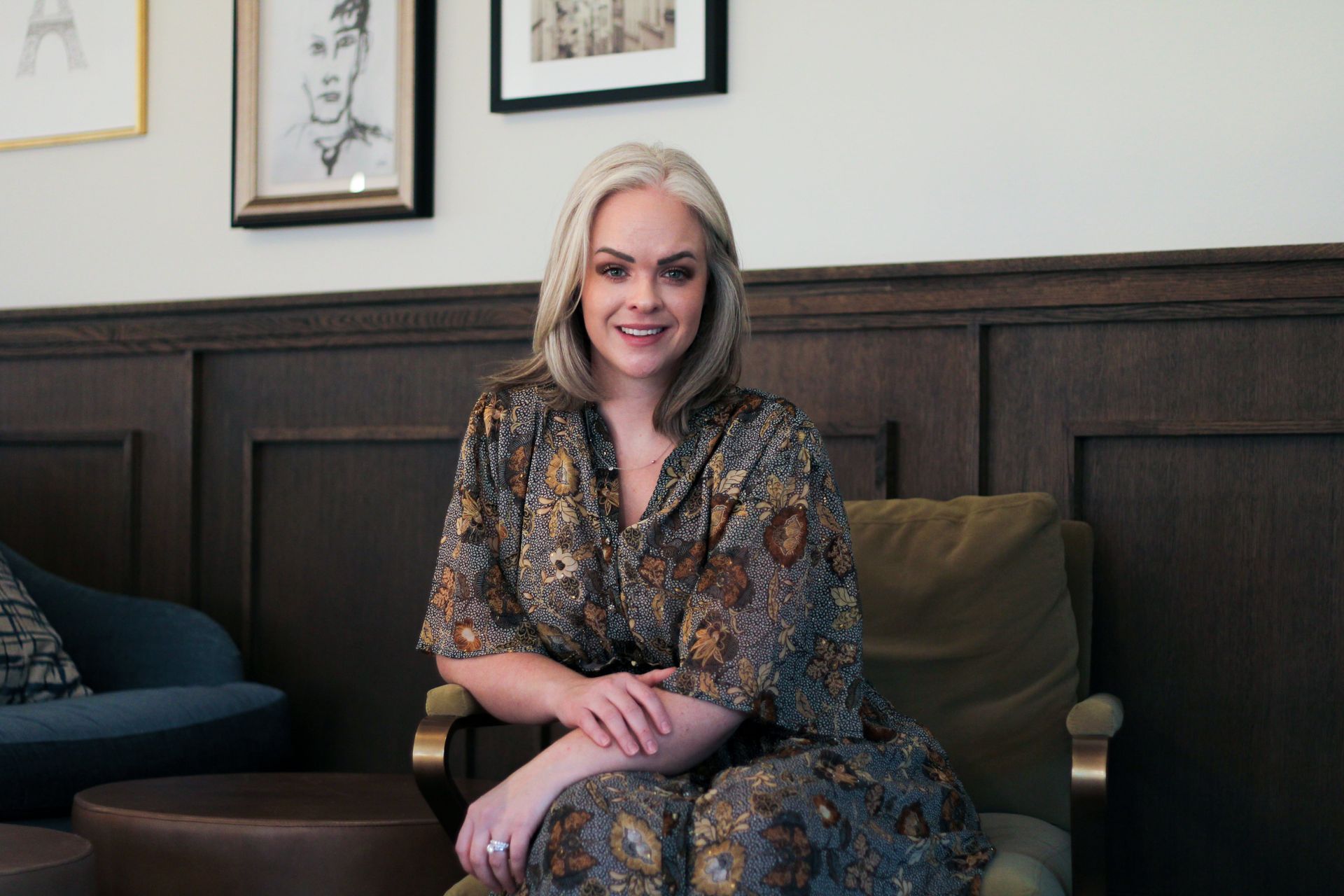 A woman is sitting in a chair with her legs crossed and smiling.