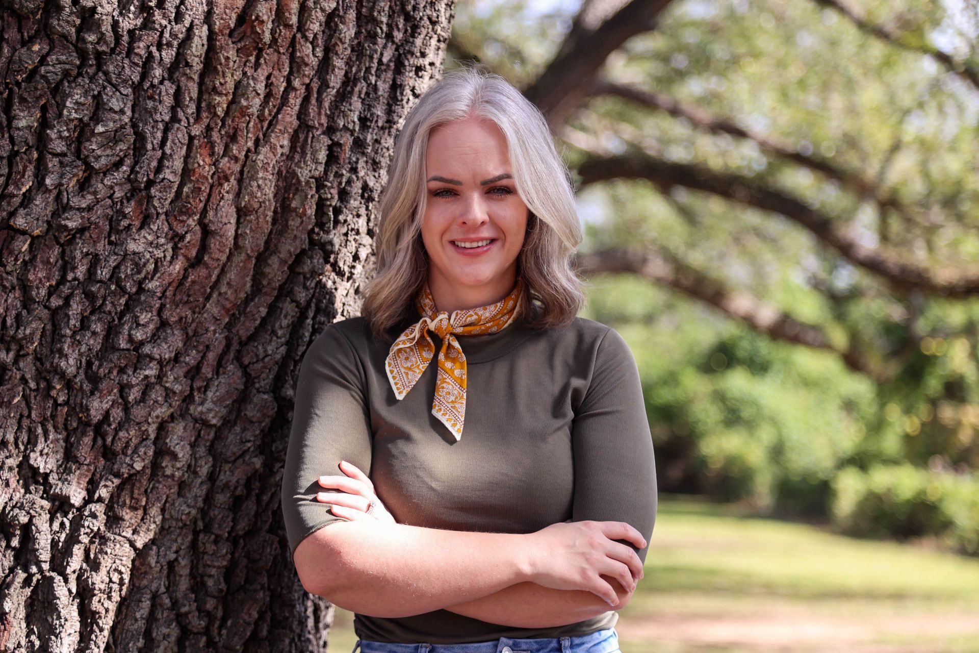 A woman is leaning against a tree with her arms crossed.