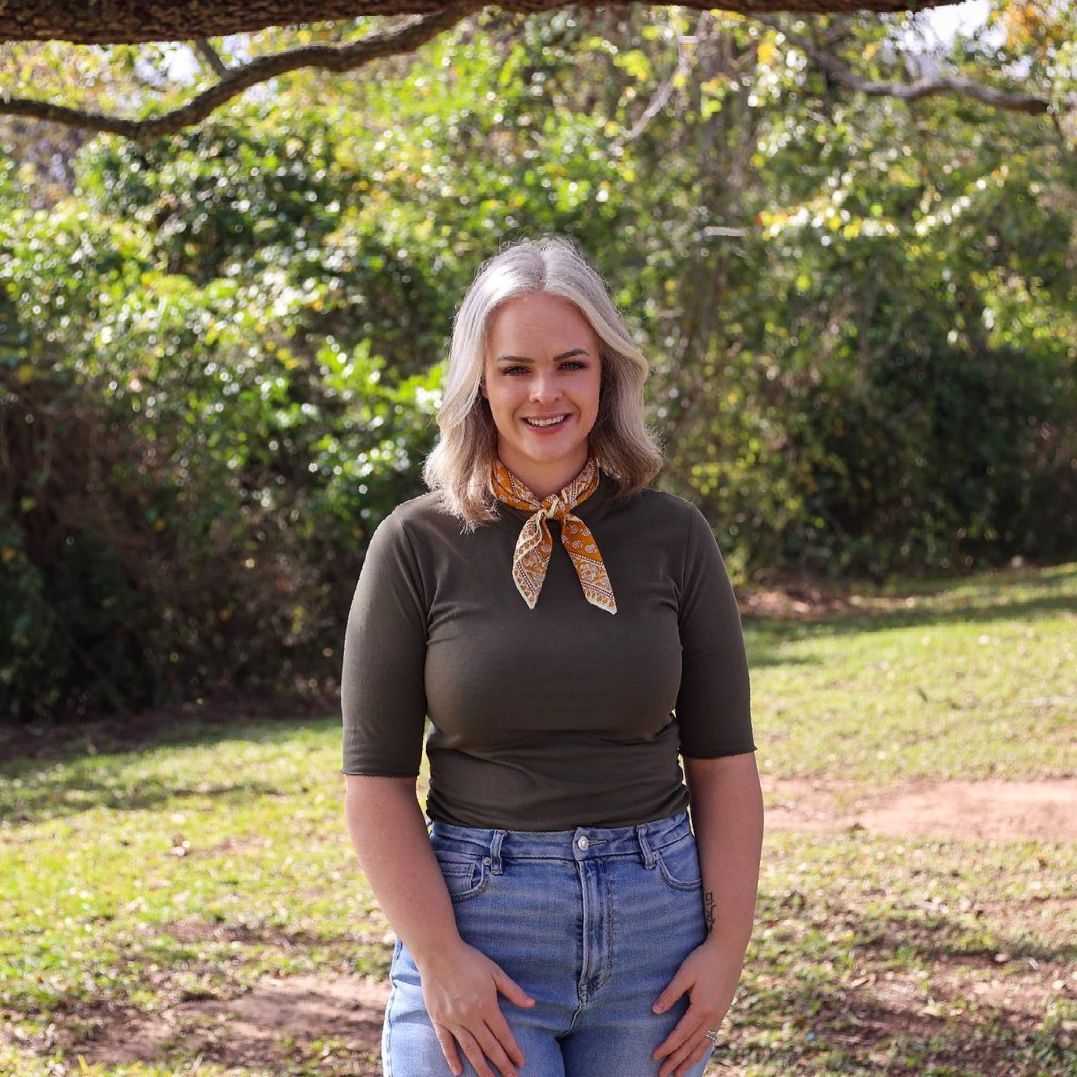 A woman wearing a green shirt and blue jeans is standing in a park.