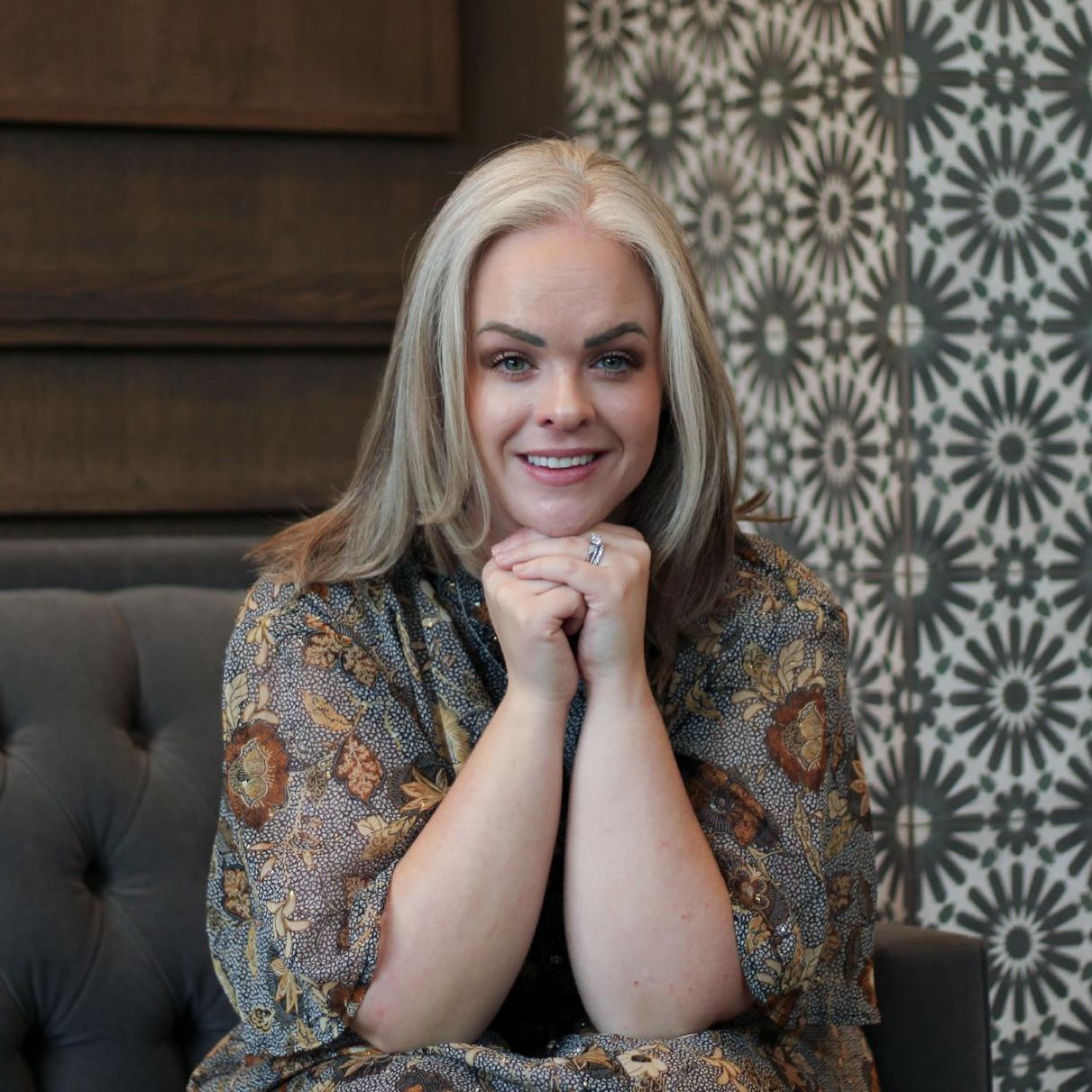 A woman is sitting on a couch with her hands folded and smiling