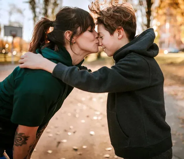 A woman and a boy are kissing in a park.