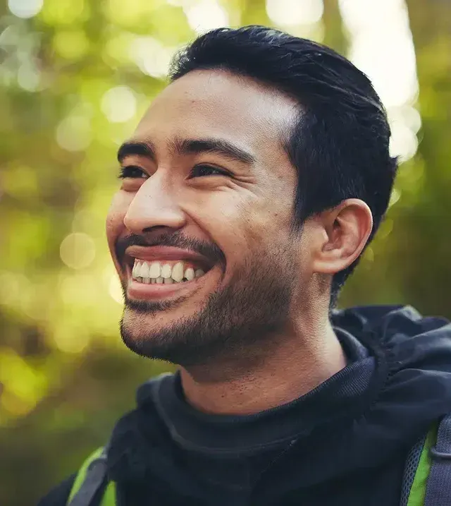 A man with a beard is smiling and wearing a backpack.