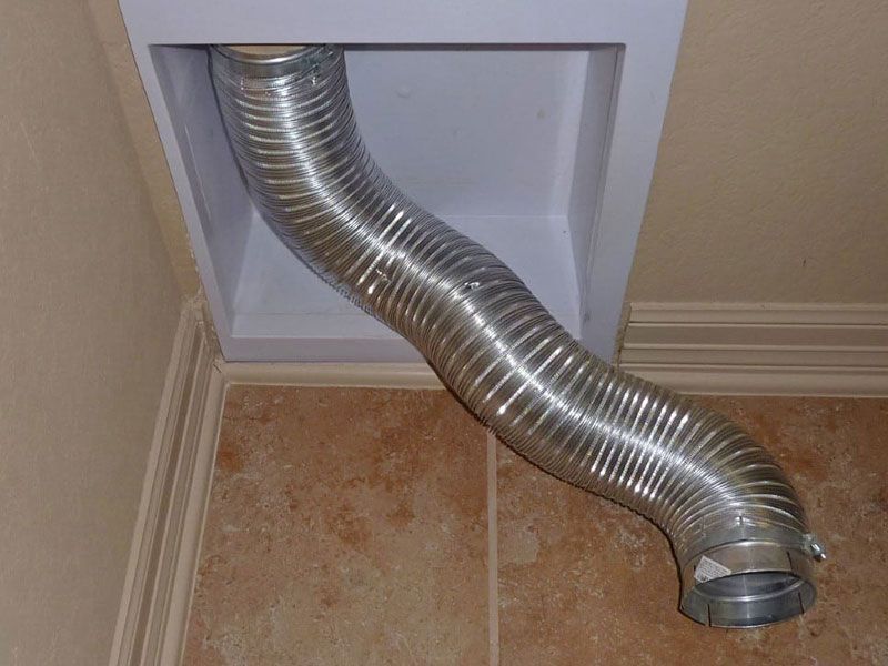 A metal hose is coming out of a hole in the wall.