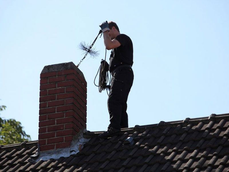 A man is standing on a roof next to a chimney