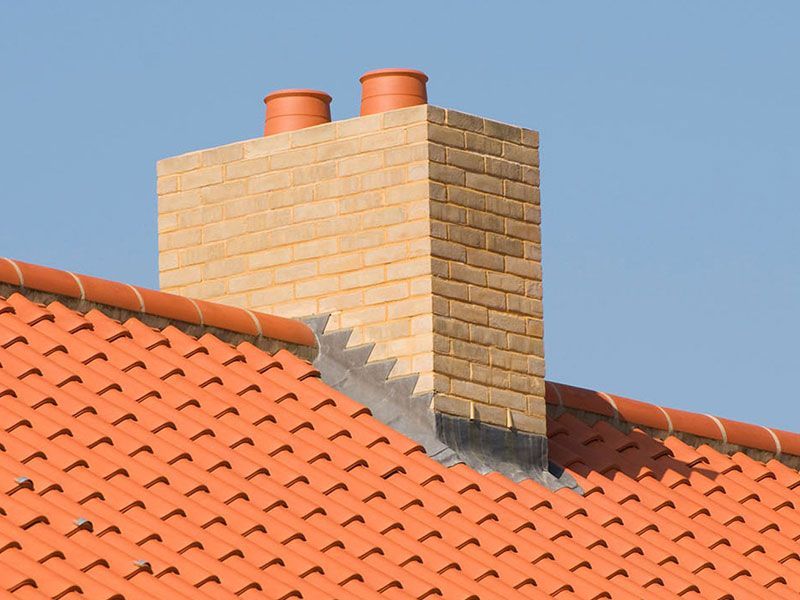 A brick chimney on top of a red tiled roof