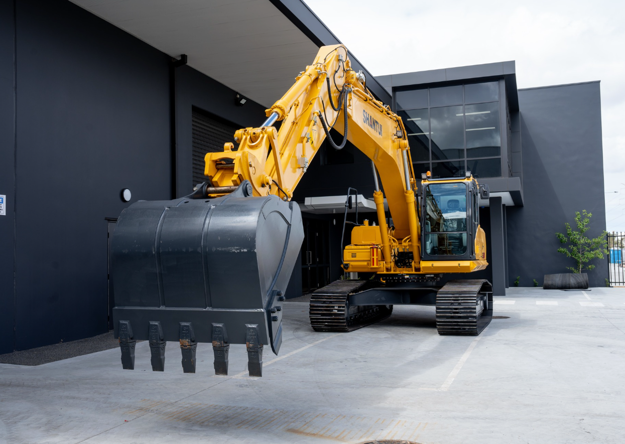 Yellow excavator with a large black bucket, parked in front of a dark building.— Northern Heavy Machinery in Mount Louisa, QLD