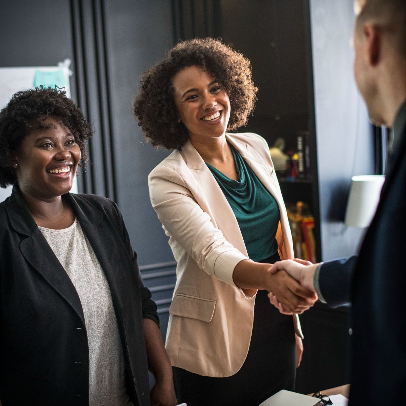 Two women are shaking hands with a man in an office.