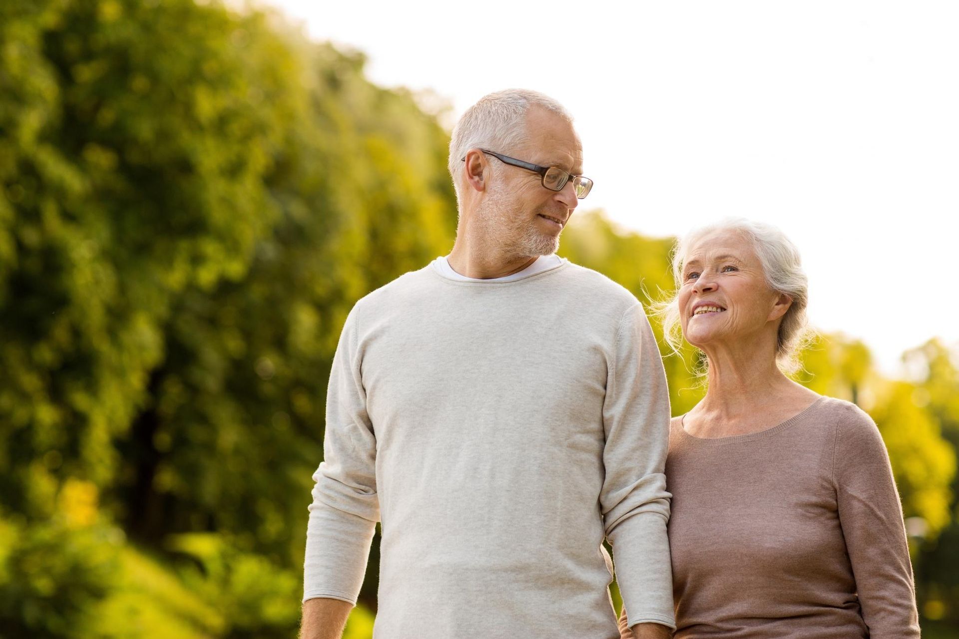 An elderly couple is walking in a park holding hands.