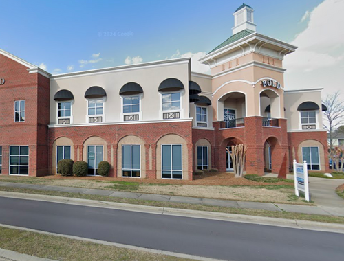 A large brick building with a lot of windows and a for sale sign in front of it